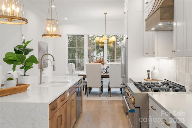 kitchen with pendant lighting, white cabinetry, sink, custom exhaust hood, and stainless steel appliances