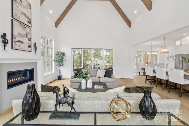 living room with a notable chandelier, high vaulted ceiling, beamed ceiling, and light wood-type flooring