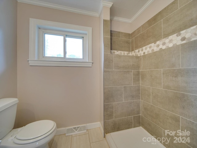 bathroom with tile patterned floors, crown molding, toilet, and tiled shower