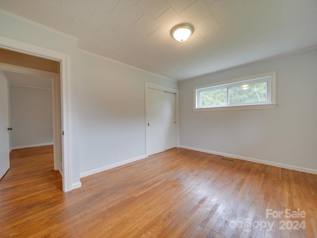 unfurnished bedroom with a closet, crown molding, and hardwood / wood-style floors