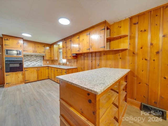 kitchen with ventilation hood, black oven, stainless steel microwave, and light hardwood / wood-style floors