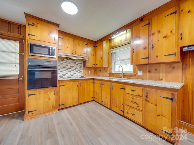 kitchen featuring light wood-type flooring, tasteful backsplash, sink, wood walls, and black appliances