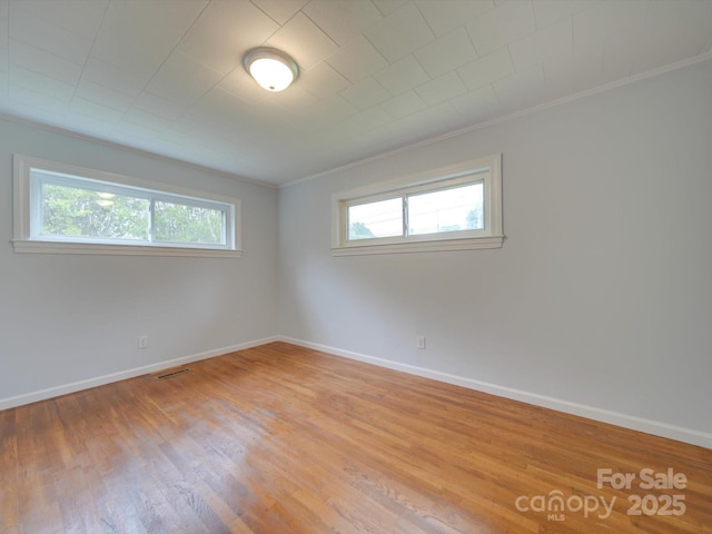 empty room featuring crown molding, wood finished floors, visible vents, and baseboards