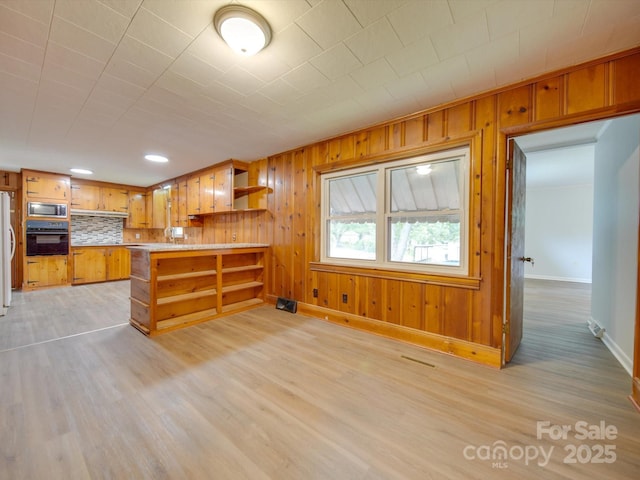 kitchen with a peninsula, light wood-style floors, black oven, open shelves, and stainless steel microwave