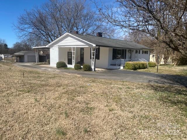 ranch-style home featuring covered porch, a garage, an outdoor structure, a front lawn, and a chimney