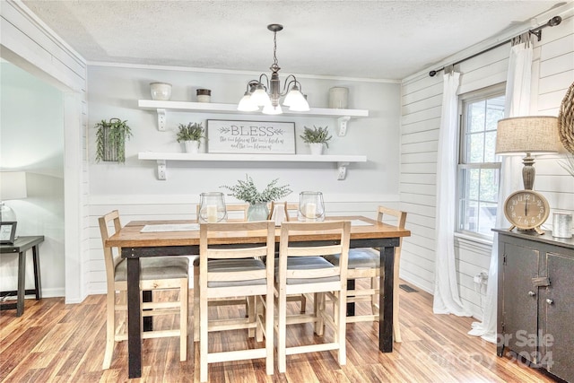 dining room featuring a textured ceiling, light hardwood / wood-style floors, wooden walls, crown molding, and a chandelier