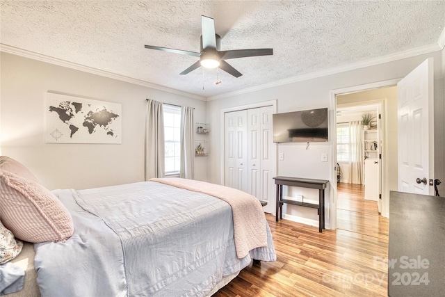 bedroom with ceiling fan, a textured ceiling, light wood-type flooring, ornamental molding, and a closet