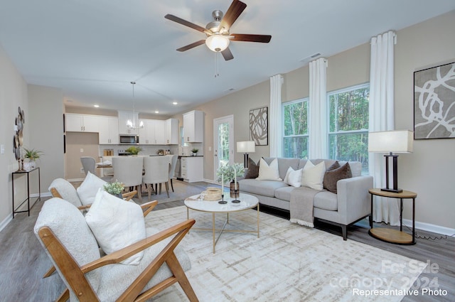 living room featuring ceiling fan with notable chandelier and light hardwood / wood-style floors