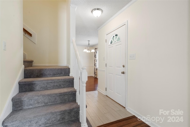 foyer entrance with a chandelier, a textured ceiling, hardwood / wood-style flooring, and crown molding