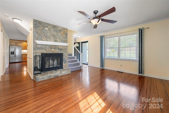 unfurnished living room with a stone fireplace, a textured ceiling, crown molding, ceiling fan, and hardwood / wood-style floors