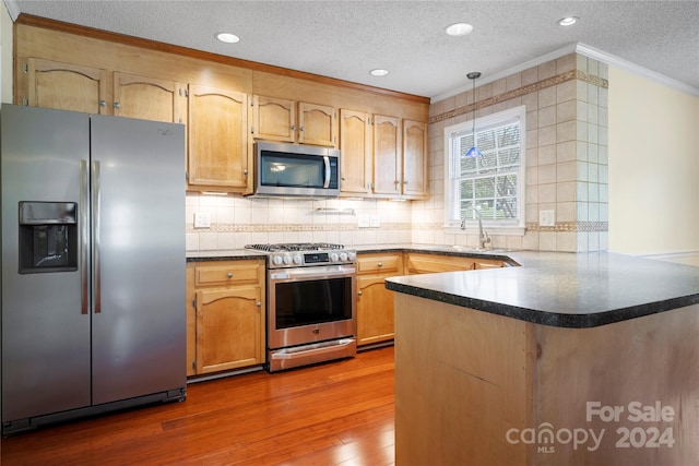 kitchen with appliances with stainless steel finishes, kitchen peninsula, crown molding, dark hardwood / wood-style floors, and sink