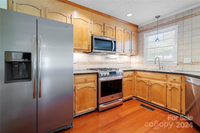 kitchen featuring hanging light fixtures, stainless steel appliances, light wood-type flooring, ornamental molding, and sink