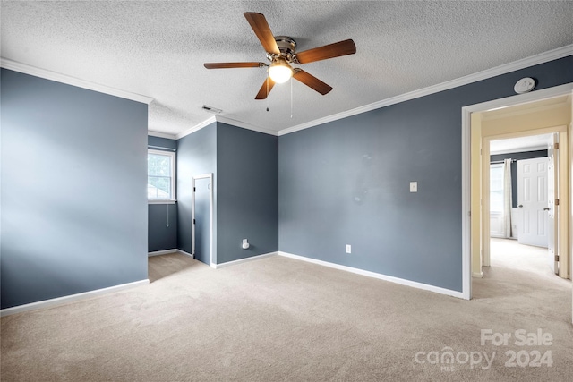 unfurnished room featuring a textured ceiling, ornamental molding, light carpet, and ceiling fan