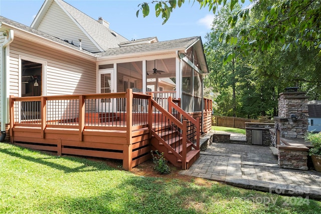 deck with a stone fireplace, a lawn, a sunroom, ceiling fan, and a patio area