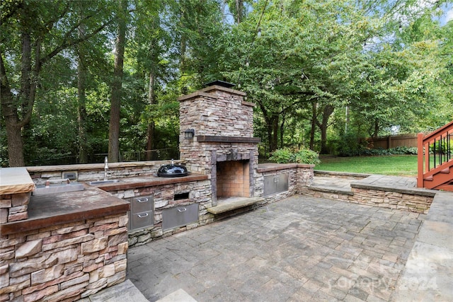 view of patio / terrace featuring an outdoor stone fireplace, an outdoor kitchen, and sink