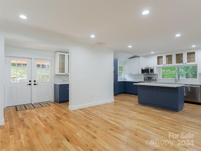 kitchen featuring appliances with stainless steel finishes, white cabinets, a kitchen island, blue cabinetry, and light wood-type flooring