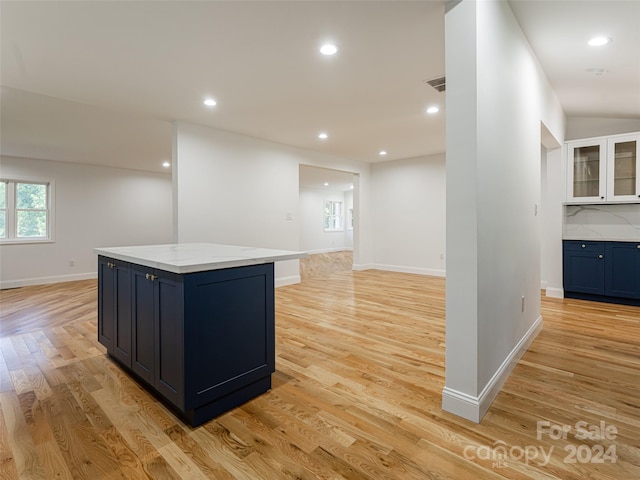 kitchen with a center island, white cabinets, vaulted ceiling, light hardwood / wood-style flooring, and light stone countertops