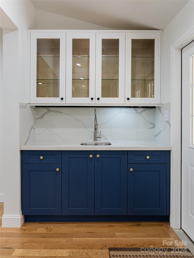 bar featuring light wood-type flooring, sink, blue cabinetry, and tasteful backsplash