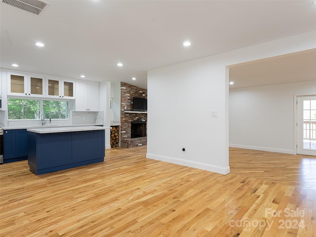 kitchen featuring tasteful backsplash, a kitchen island, a brick fireplace, white cabinetry, and light wood-type flooring