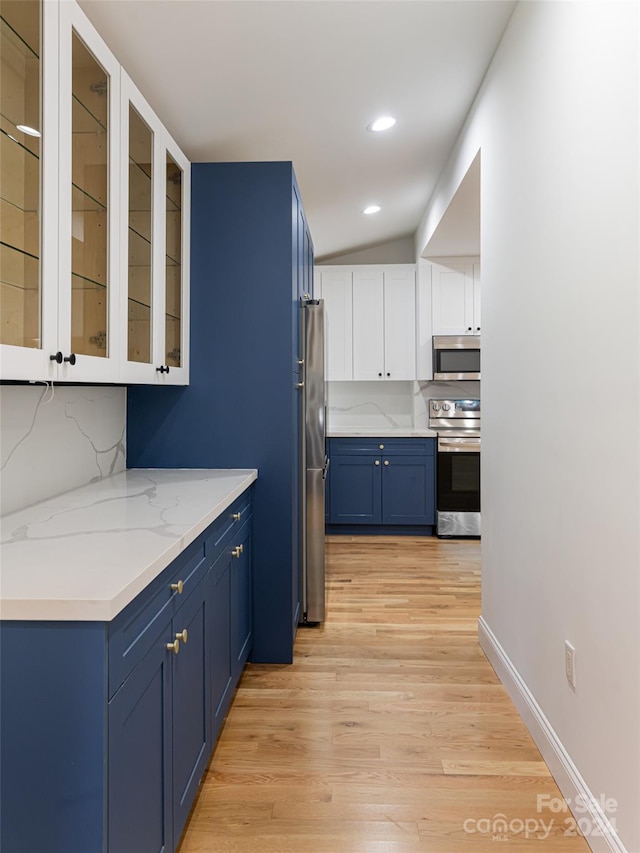 kitchen with appliances with stainless steel finishes, light hardwood / wood-style floors, white cabinetry, light stone countertops, and blue cabinetry