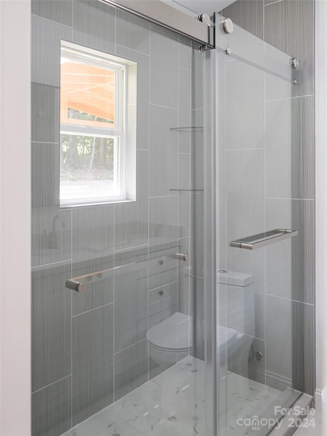 bathroom featuring a shower with door and toilet