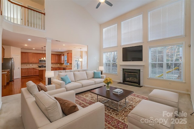 carpeted living room featuring ceiling fan with notable chandelier and high vaulted ceiling