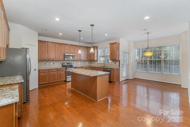 kitchen featuring a kitchen island, appliances with stainless steel finishes, pendant lighting, and light hardwood / wood-style floors