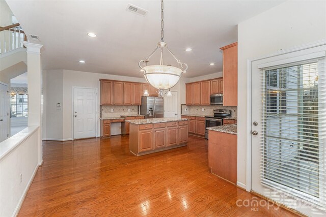 kitchen with hanging light fixtures, appliances with stainless steel finishes, a center island, and light stone counters