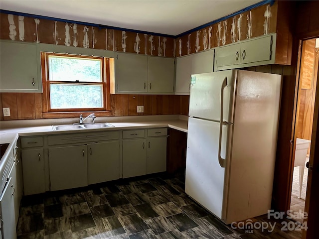 kitchen featuring white fridge, wood walls, and sink