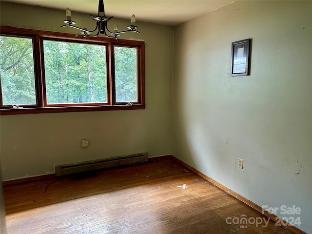 spare room with hardwood / wood-style flooring, a baseboard radiator, and a chandelier