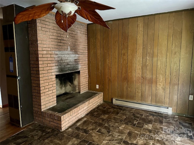 unfurnished living room with ceiling fan, a baseboard heating unit, a brick fireplace, and wood walls