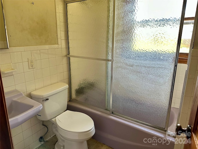 bathroom featuring toilet, combined bath / shower with glass door, tile patterned floors, and tile walls