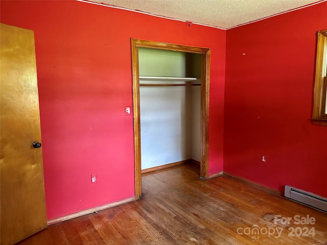 unfurnished bedroom featuring a baseboard radiator, a textured ceiling, wood-type flooring, and a closet