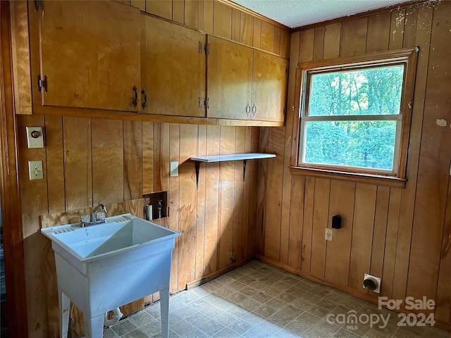 laundry area with cabinets, a textured ceiling, wooden walls, and sink