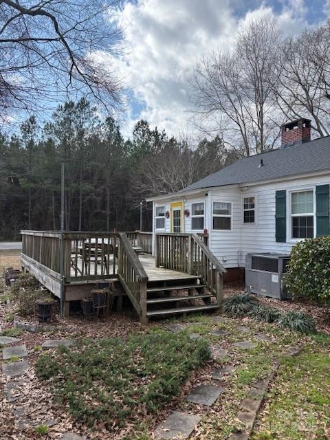 back of property featuring a chimney, a deck, and roof with shingles