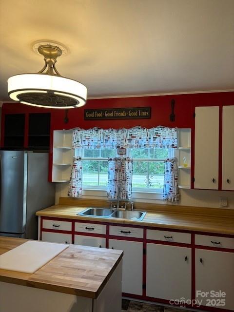 kitchen with white cabinets, decorative light fixtures, freestanding refrigerator, open shelves, and a sink