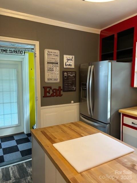 kitchen with wainscoting, stainless steel fridge with ice dispenser, dark floors, ornamental molding, and wooden counters