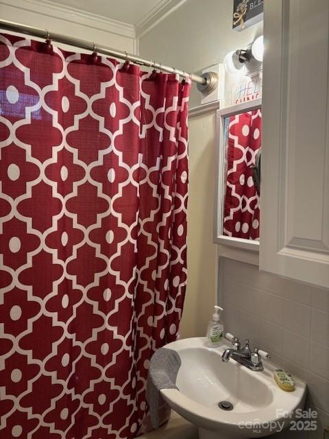 bathroom with ornamental molding, decorative backsplash, a sink, and a shower with shower curtain