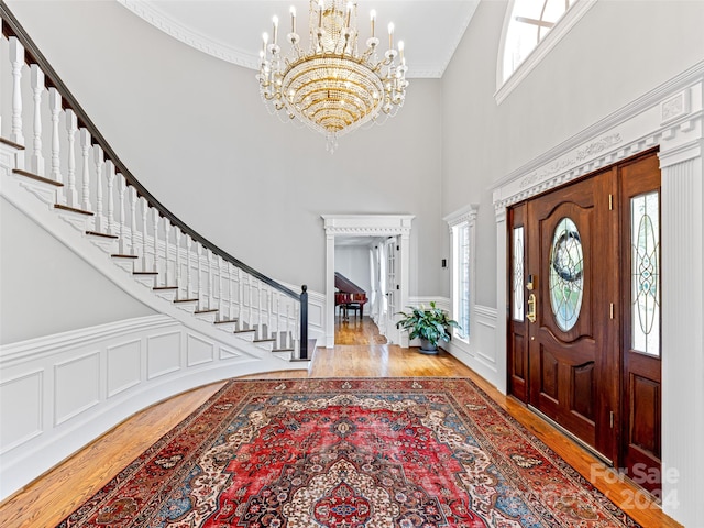 entrance foyer featuring light wood-type flooring, crown molding, a towering ceiling, and a notable chandelier