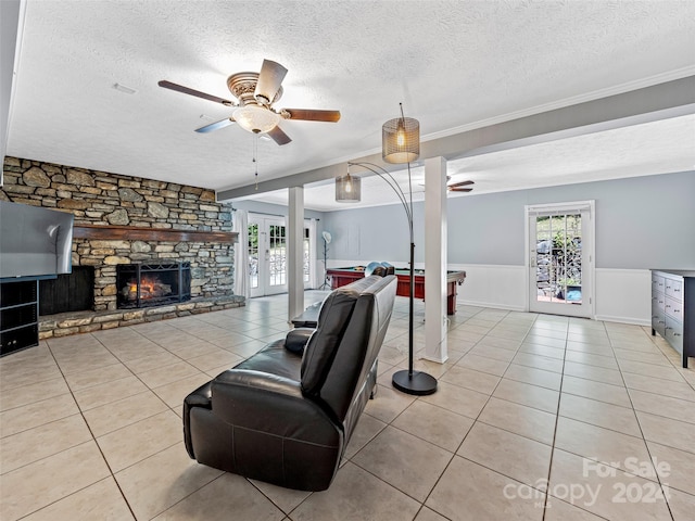 tiled living room with a stone fireplace, ceiling fan, billiards, and a textured ceiling