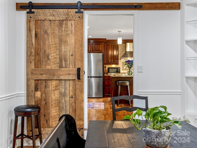 kitchen featuring appliances with stainless steel finishes, hanging light fixtures, a barn door, wood-type flooring, and wall chimney range hood