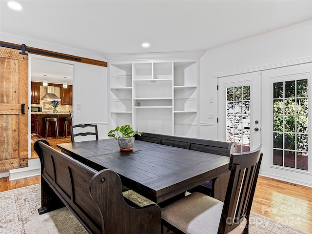 dining room featuring light hardwood / wood-style flooring, crown molding, and a barn door