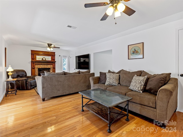 living room featuring a brick fireplace, light hardwood / wood-style floors, and ceiling fan