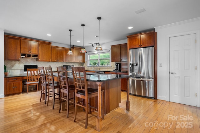 kitchen featuring appliances with stainless steel finishes, a breakfast bar, pendant lighting, light hardwood / wood-style flooring, and a kitchen island