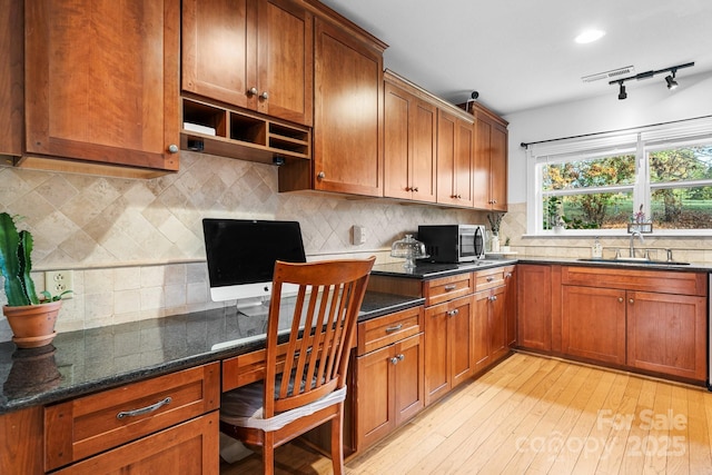 kitchen with track lighting, sink, built in desk, light hardwood / wood-style flooring, and dark stone countertops