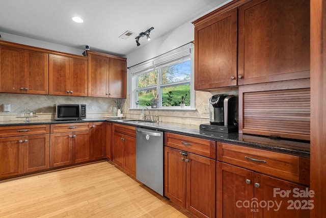 kitchen with tasteful backsplash, dark stone counters, stainless steel appliances, sink, and light hardwood / wood-style flooring