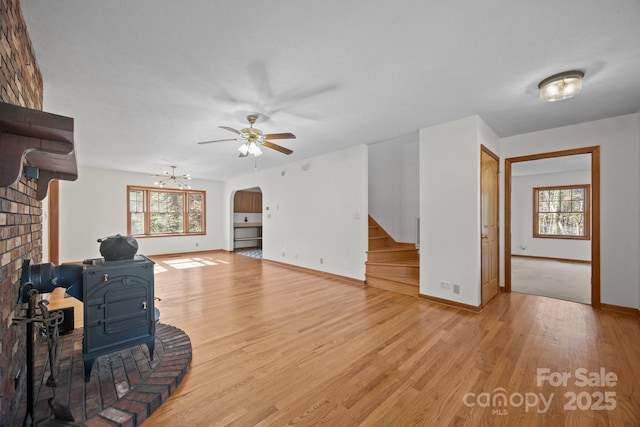 unfurnished living room with ceiling fan, plenty of natural light, a wood stove, and light hardwood / wood-style flooring