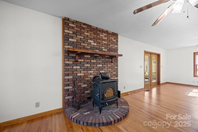 unfurnished living room with ceiling fan, a wood stove, wood-type flooring, and french doors