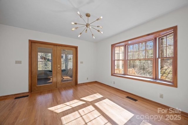 unfurnished room featuring light wood-type flooring, french doors, and an inviting chandelier