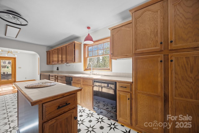 kitchen featuring a center island, sink, black dishwasher, hanging light fixtures, and tile counters